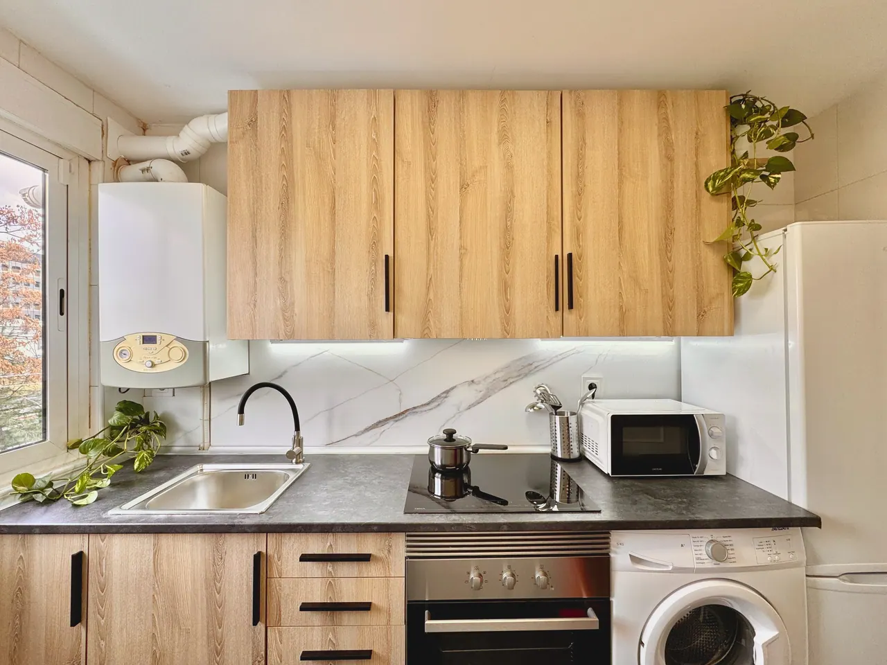 Cocina con muebles de madera, placa, horno, microondas y lavadora (foto 2 de 7)