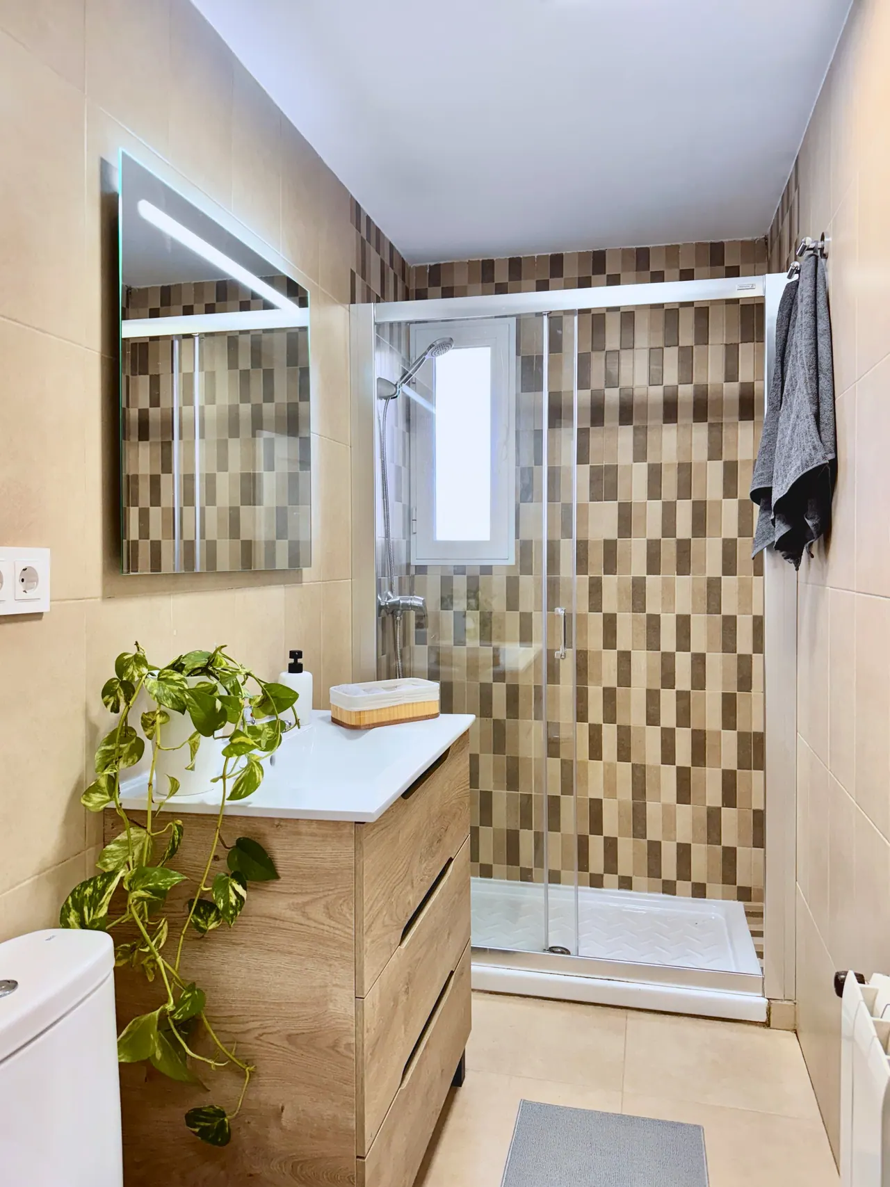 Baño con mueble de lavabo de madera, espejo iluminado y ducha con mampara (foto 3 de 7)