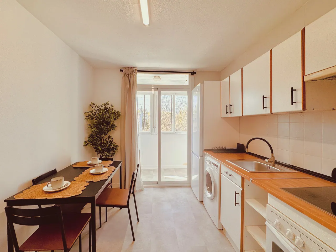 Cocina alargada con encimera de madera, mesa de comedor y puerta a la terraza al fondo