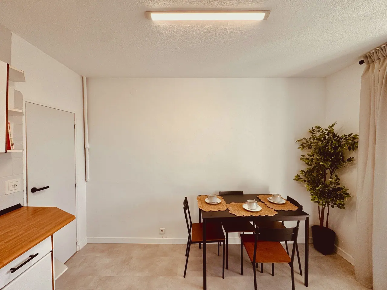 Zona de comedor con mesa de madera, cuatro sillas negras y planta (foto 3 de 9)
