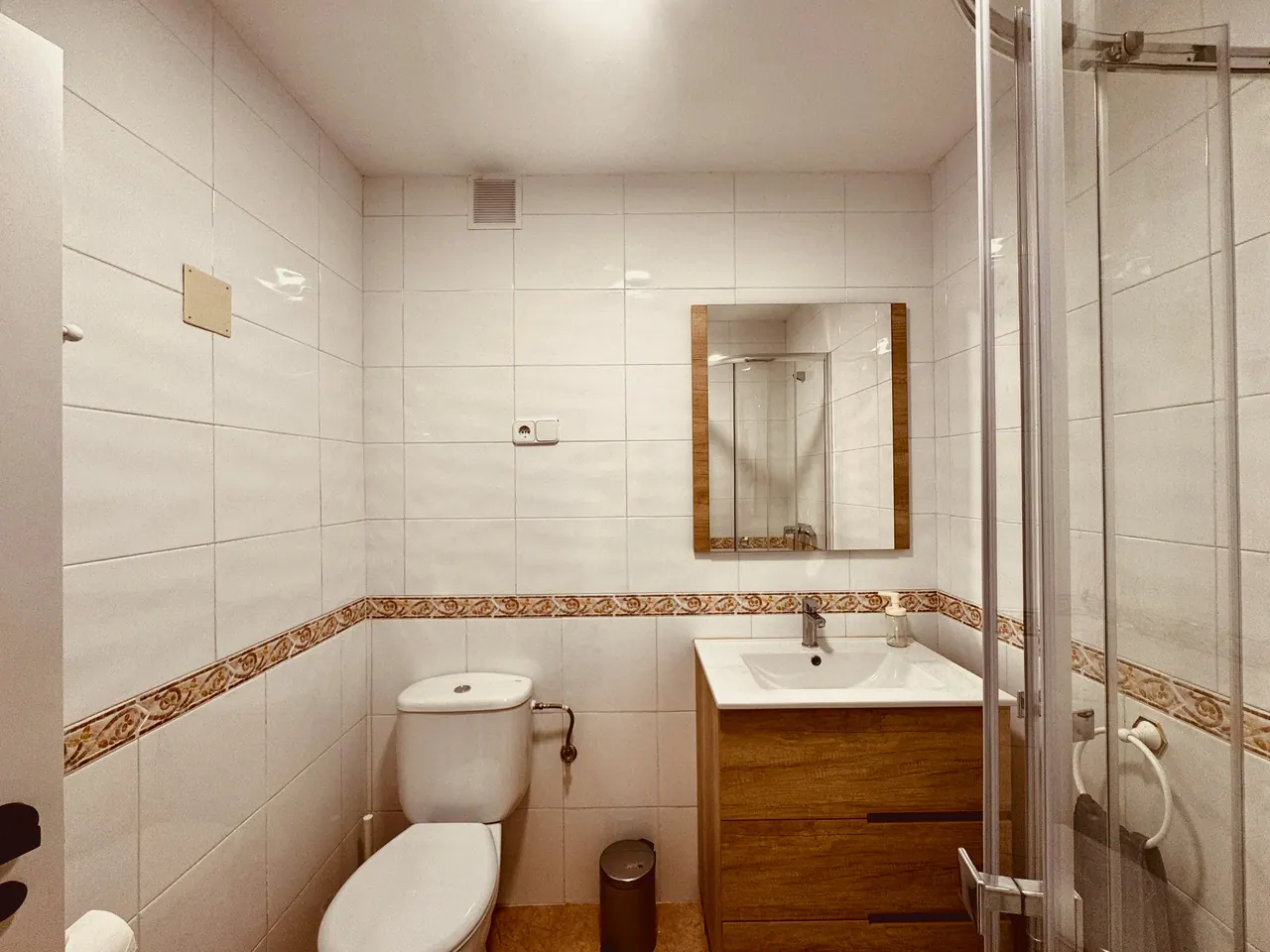 Baño con azulejo blanco, mueble de lavabo de madera, espejo e inodoro (foto 4 de 9)