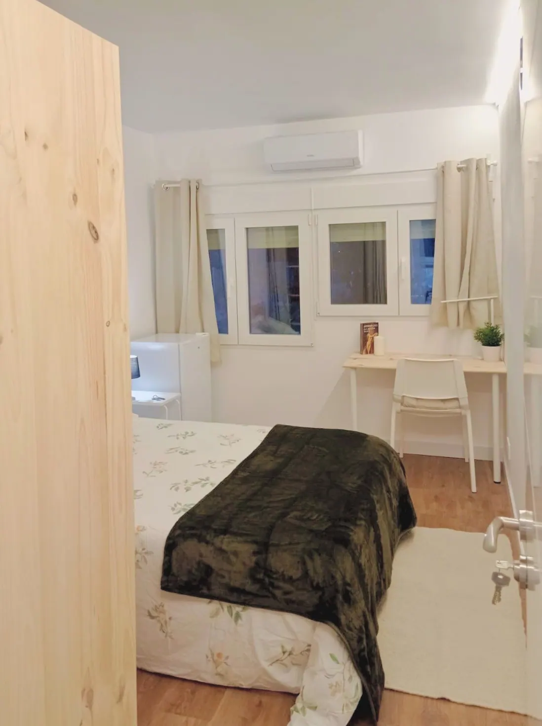Habitación con cama de matrimonio, escritorio bajo una ventana corrida y aire acondicionado