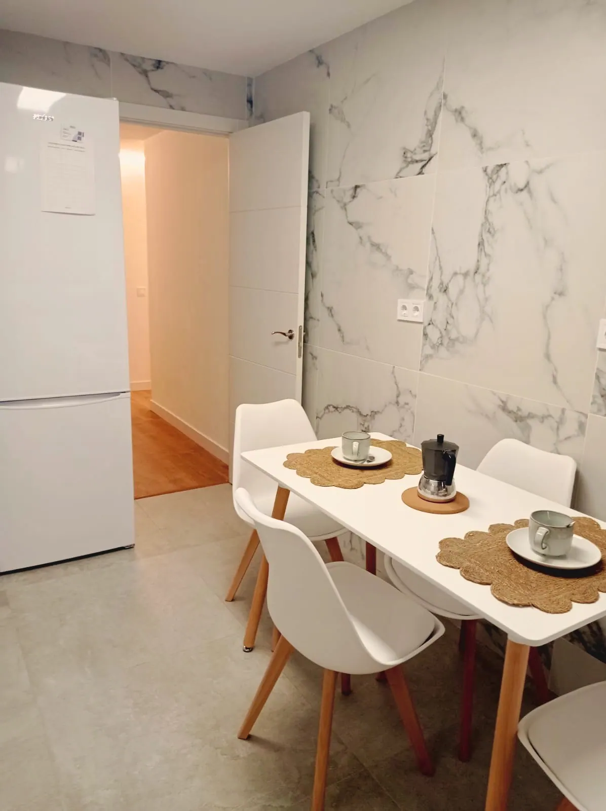 Mesa de comedor blanca con sillas y frigorífico junto a la pared de mármol (foto 2 de 8)