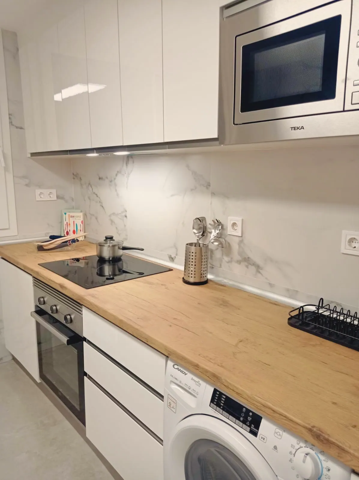 Cocina con encimera de madera, placa, horno, microondas y lavadora (foto 3 de 8)