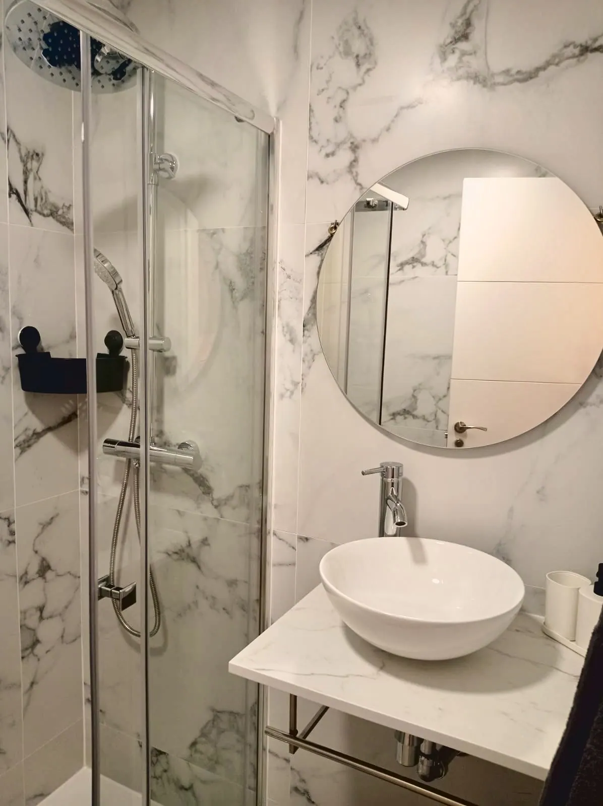 Baño de mármol con ducha de mampara, lavabo sobre repisa y espejo redondo (foto 4 de 8)