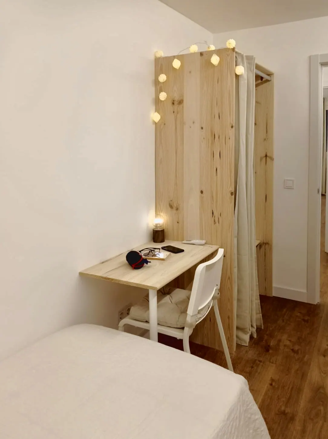 Habitación con escritorio, silla blanca y armario abierto de madera con guirnalda de luces (foto 8 de 8)