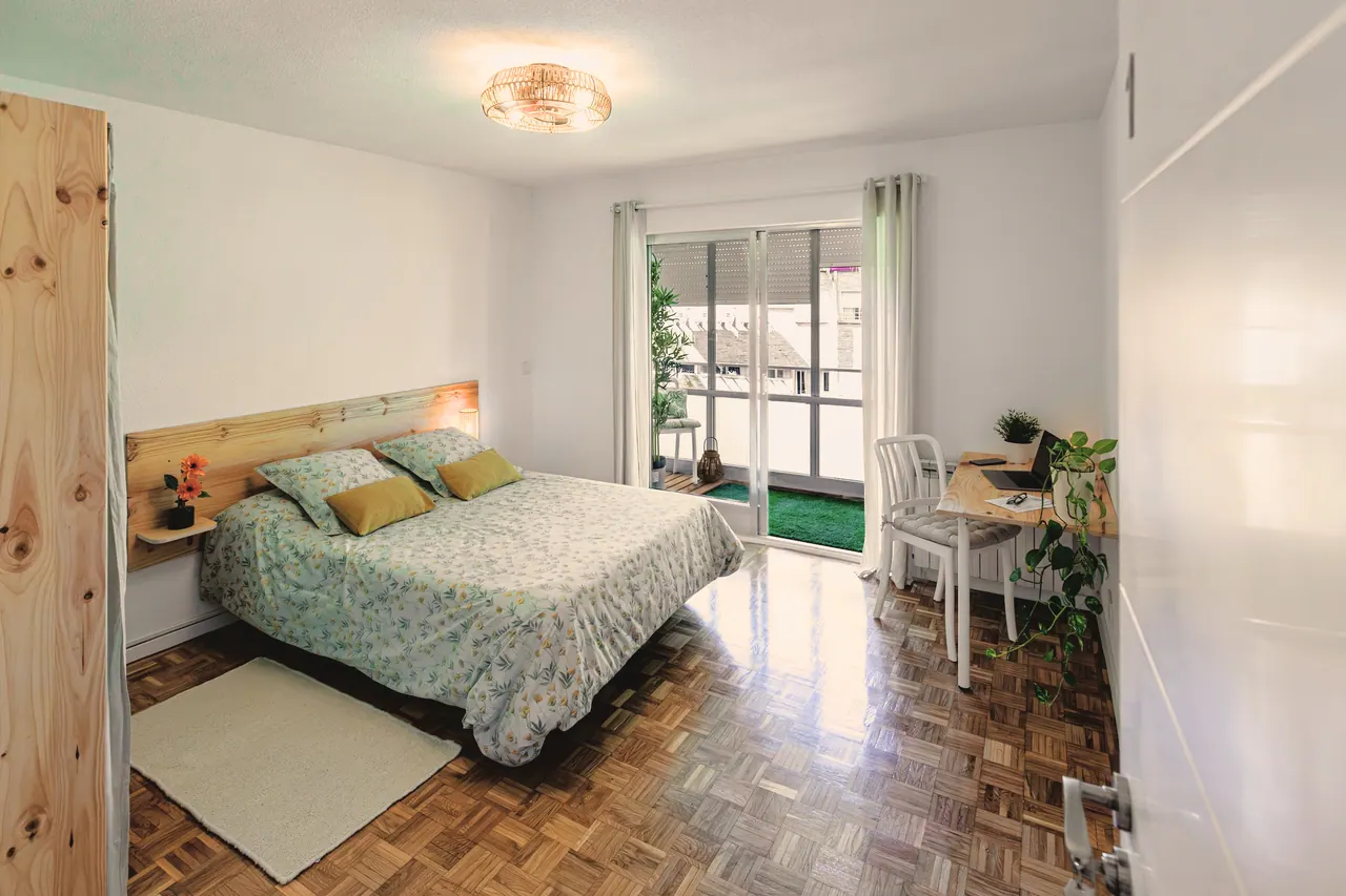 Habitación amplia con cama de matrimonio, escritorio, suelo de parqué y salida a terraza acristalada