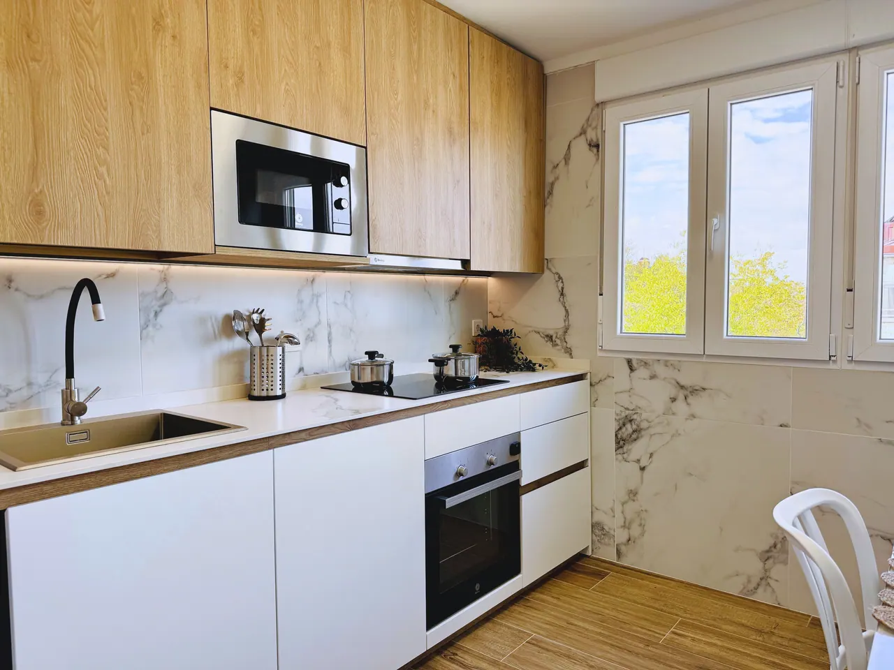 Cocina blanca con muebles altos de madera, pared de mármol, horno, microondas y ventana (foto 2 de 8)