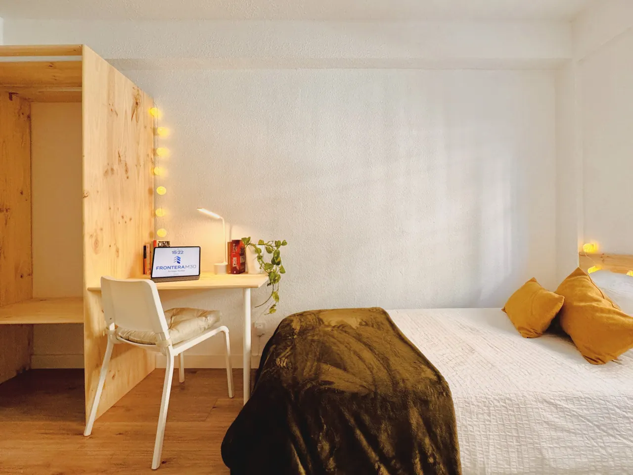 Habitación con cama, escritorio de madera, armario abierto con cortina y guirnalda de luces (foto 6 de 8)