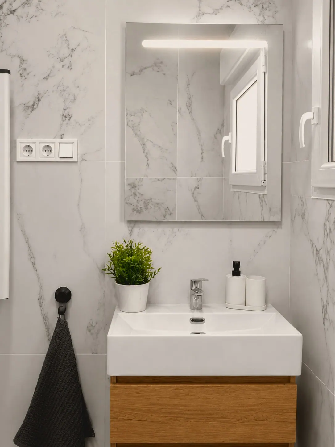 Lavabo blanco sobre mueble de madera con espejo iluminado y pared cerámica (foto 3 de 8)